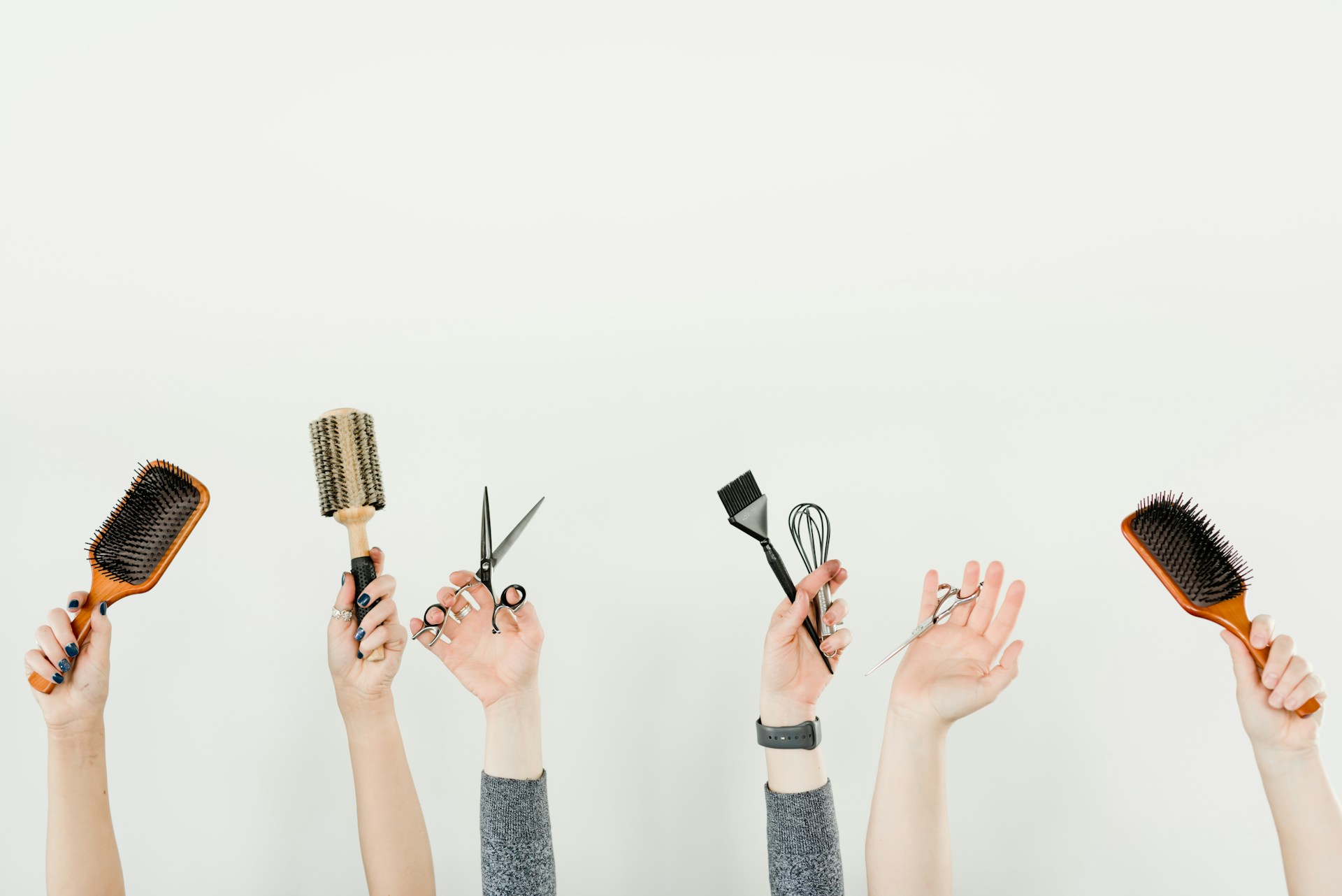 Professional hair styling tools held by skilled hands - brushes, scissors, combs